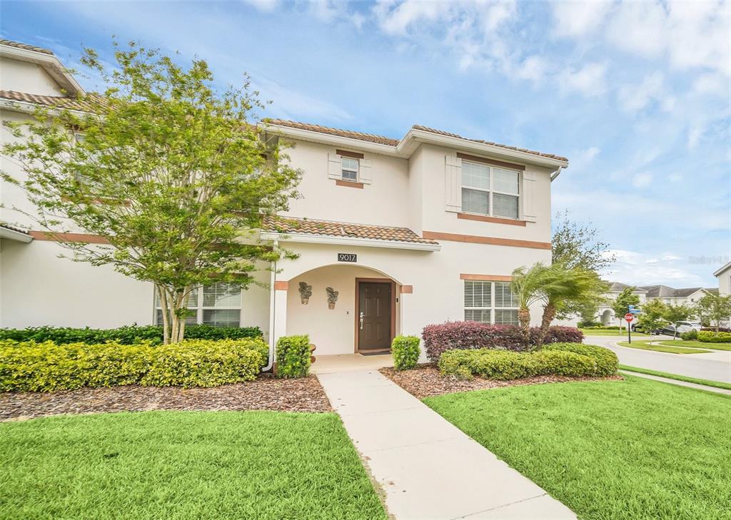A two-story townhouse exterior features a beige stucco facade, a brown front door, and landscaping — 9017 DOGLEG DRIVE, DAVENPORT, FL