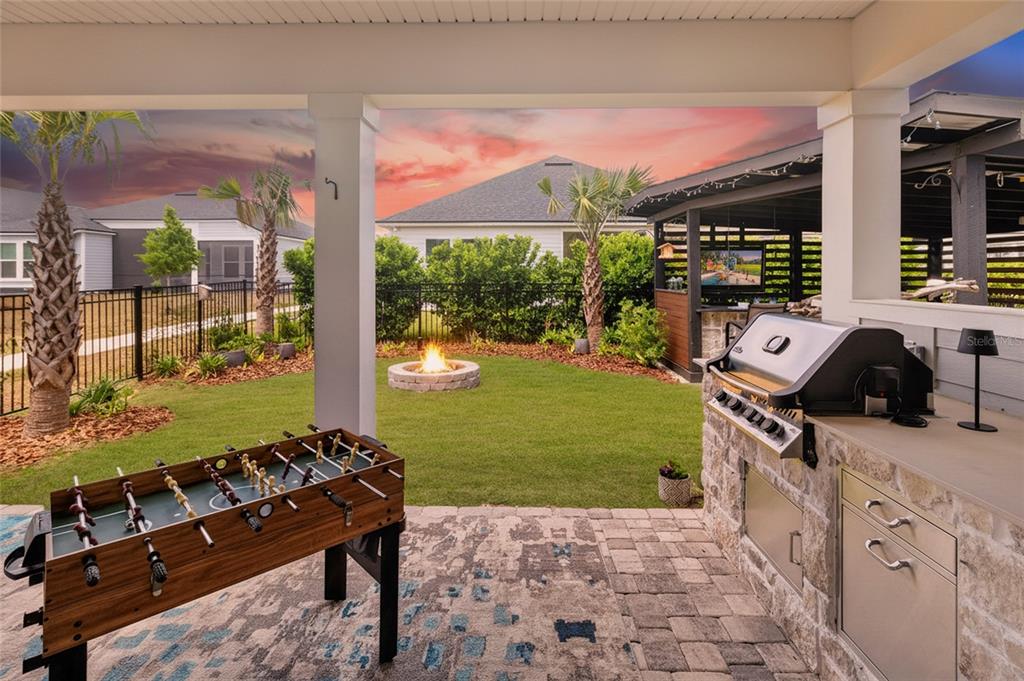 A covered patio features an outdoor kitchen, a foosball table, and a backyard fire pit — 11980 SW 31ST ROAD, GAINESVILLE, FL