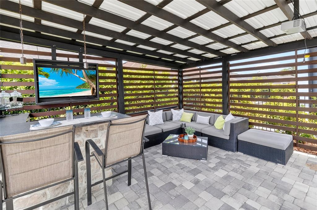 A covered outdoor patio features a stone bar, sectional seating, and a wall-mounted television — 11980 SW 31ST ROAD, GAINESVILLE, FL