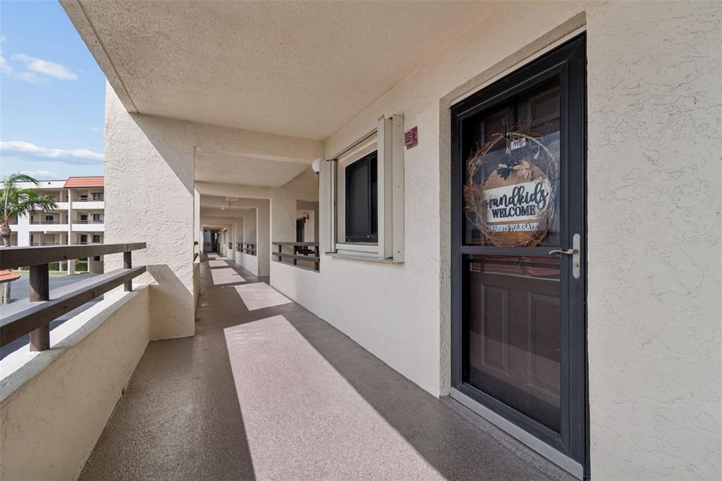 An exterior apartment walkway features a brown storm door with a decorative wreath — 103 1ST STREET E UNIT 115, ST PETERSBURG, FL