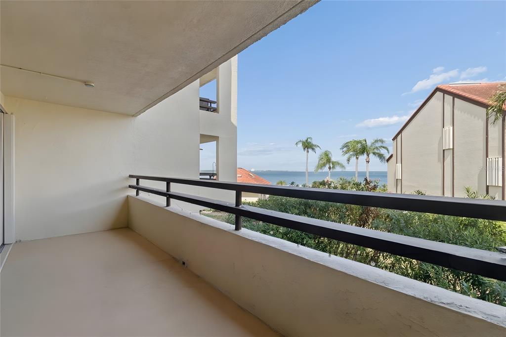A covered balcony with a dark metal railing overlooks palm trees and the ocean — 103 1ST STREET E UNIT 115, ST PETERSBURG, FL
