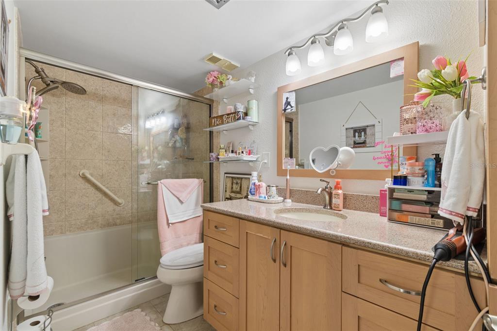A bathroom features a wood vanity with a stone countertop, a shower-tub combo, and open shelving — 103 1ST STREET E UNIT 115, ST PETERSBURG, FL