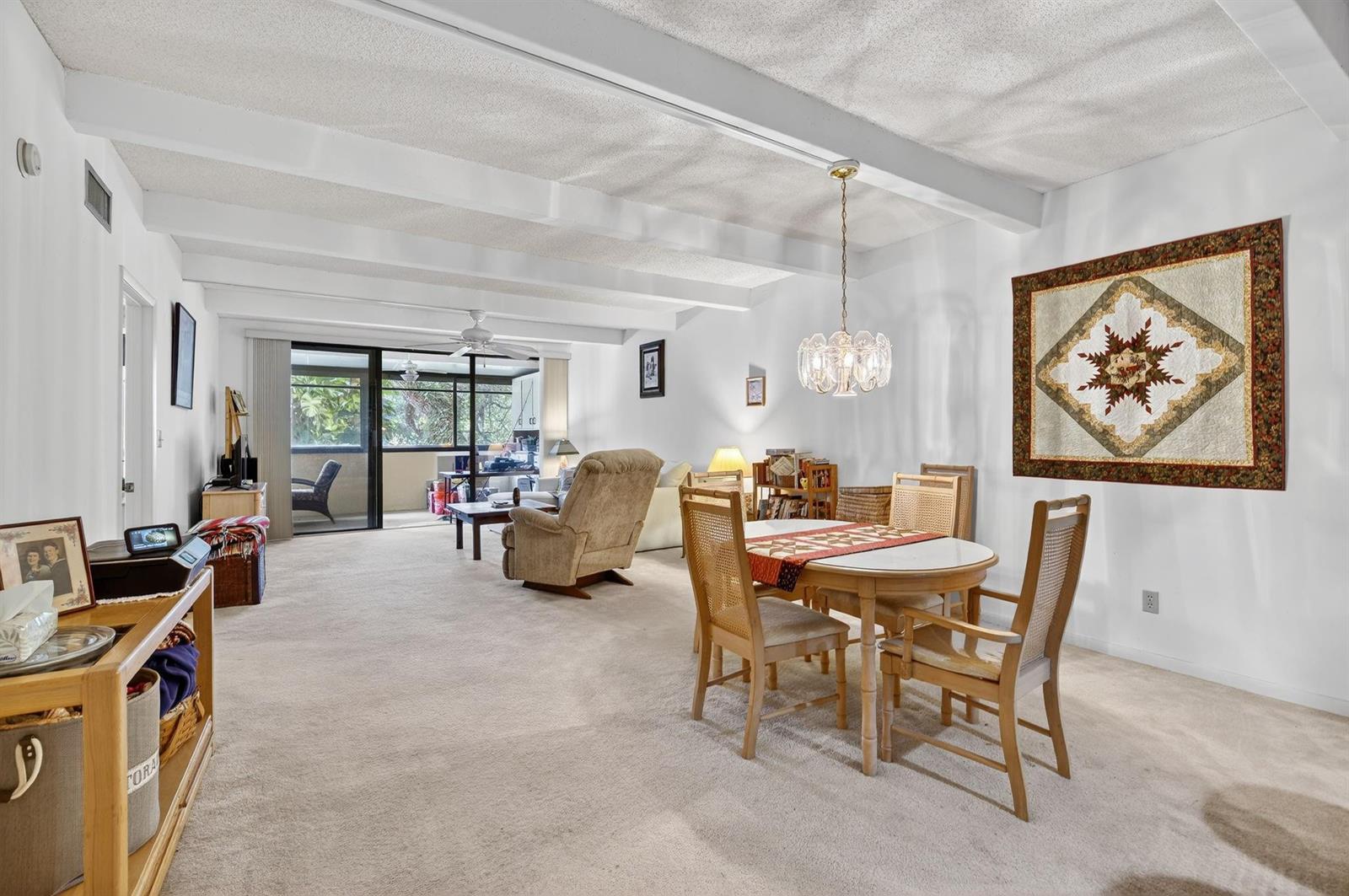 A carpeted living and dining room features white exposed ceiling beams and a glass sliding door — 240 Hammock Shore Drive # 107, Melbourne Beach FL 32951, MELBOURNE BEACH, FL