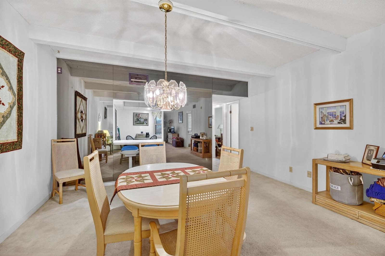 A dining room features a round table, cane-back chairs, a crystal chandelier, and mirrored walls — 240 Hammock Shore Drive # 107, Melbourne Beach FL 32951, MELBOURNE BEACH, FL