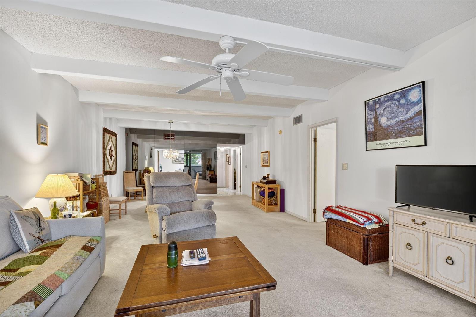 A living room features a white ceiling with exposed beams, a ceiling fan, and carpet — 240 Hammock Shore Drive # 107, Melbourne Beach FL 32951, MELBOURNE BEACH, FL