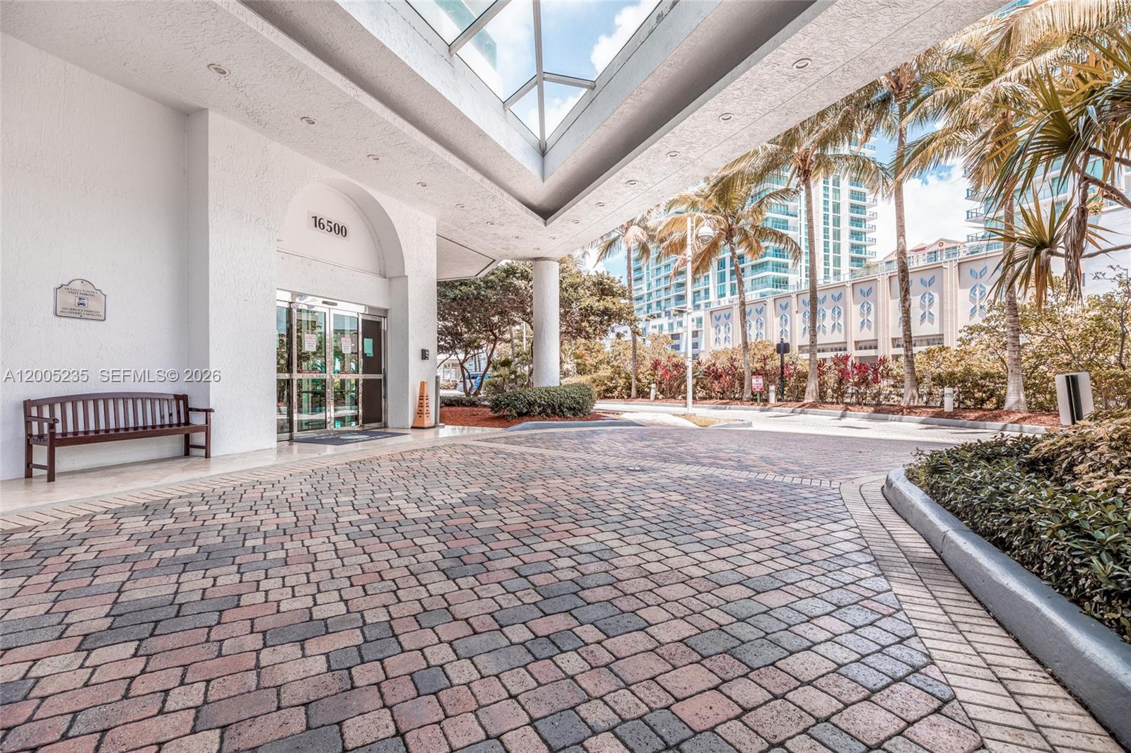 A paved driveway leads to a building entrance with a glass canopy and wooden bench — 16500 Collins Ave # 655, Sunny Isles Beach FL 33160, SUNNY ISLES BEACH, FL