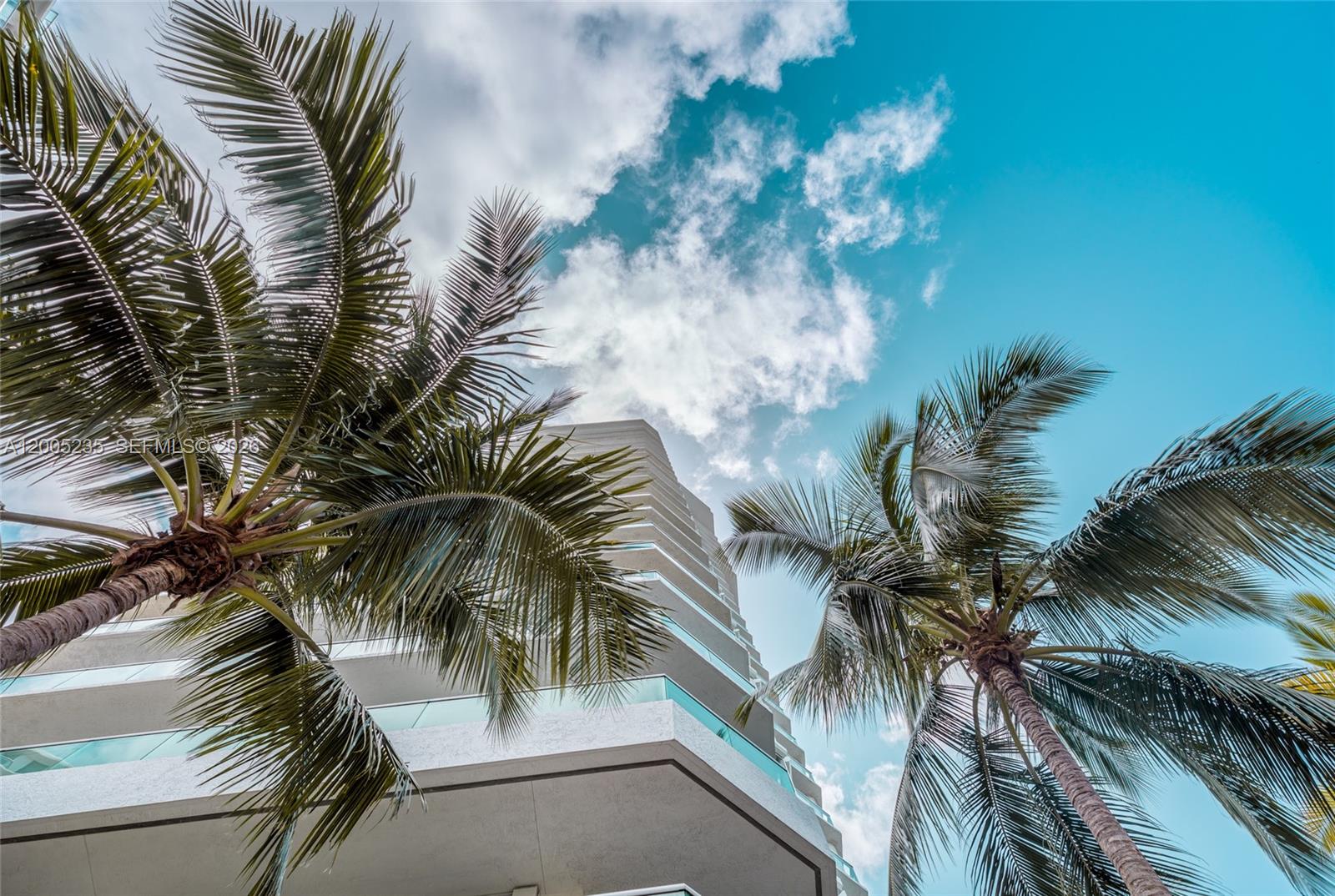 A low-angle view of a modern multi-story building framed by two palm trees — 16500 Collins Ave # 655, Sunny Isles Beach FL 33160, SUNNY ISLES BEACH, FL