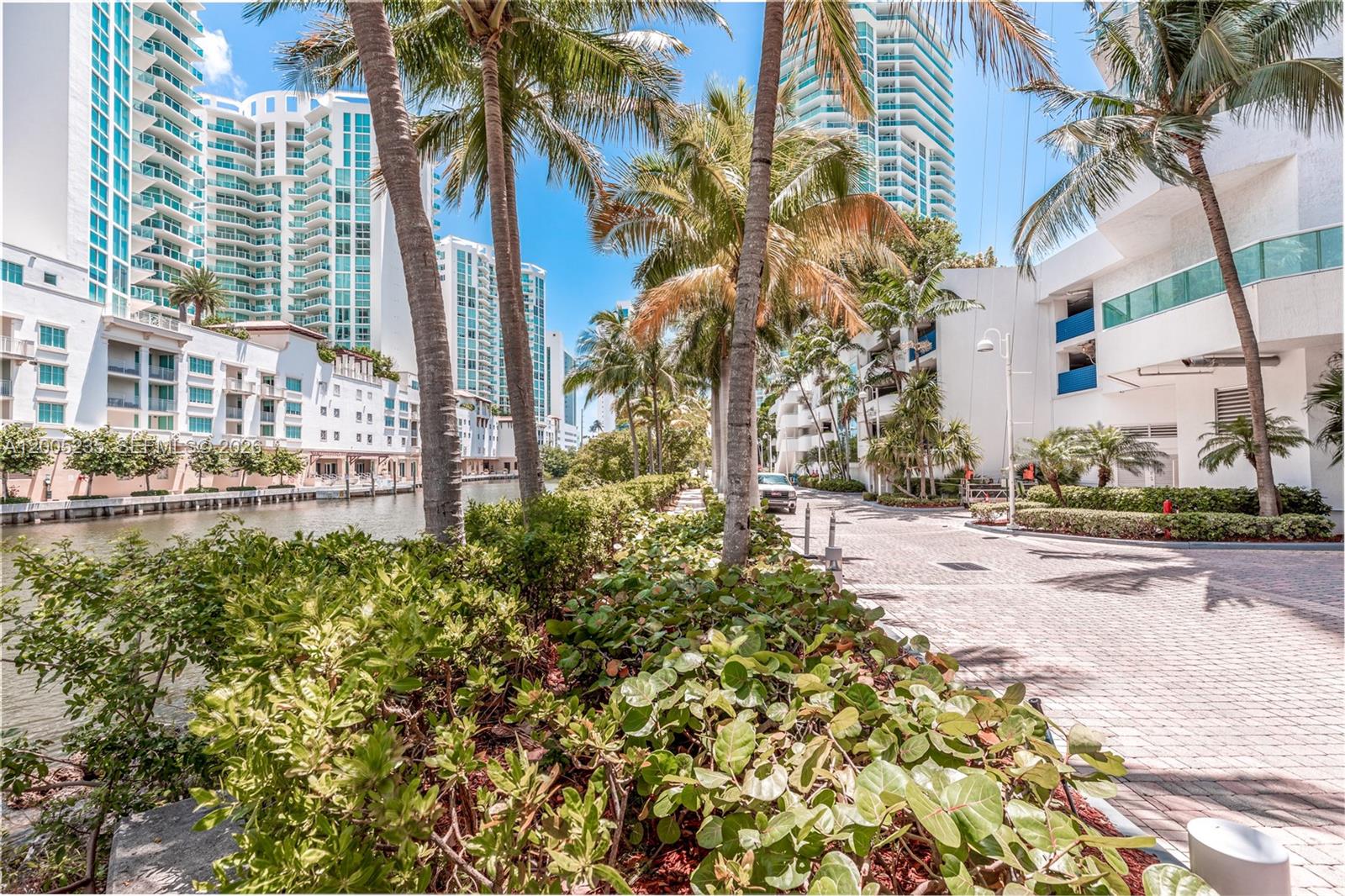 A paved walkway runs alongside a canal lined with palm trees and modern high-rise buildings — 16500 Collins Ave # 655, Sunny Isles Beach FL 33160, SUNNY ISLES BEACH, FL