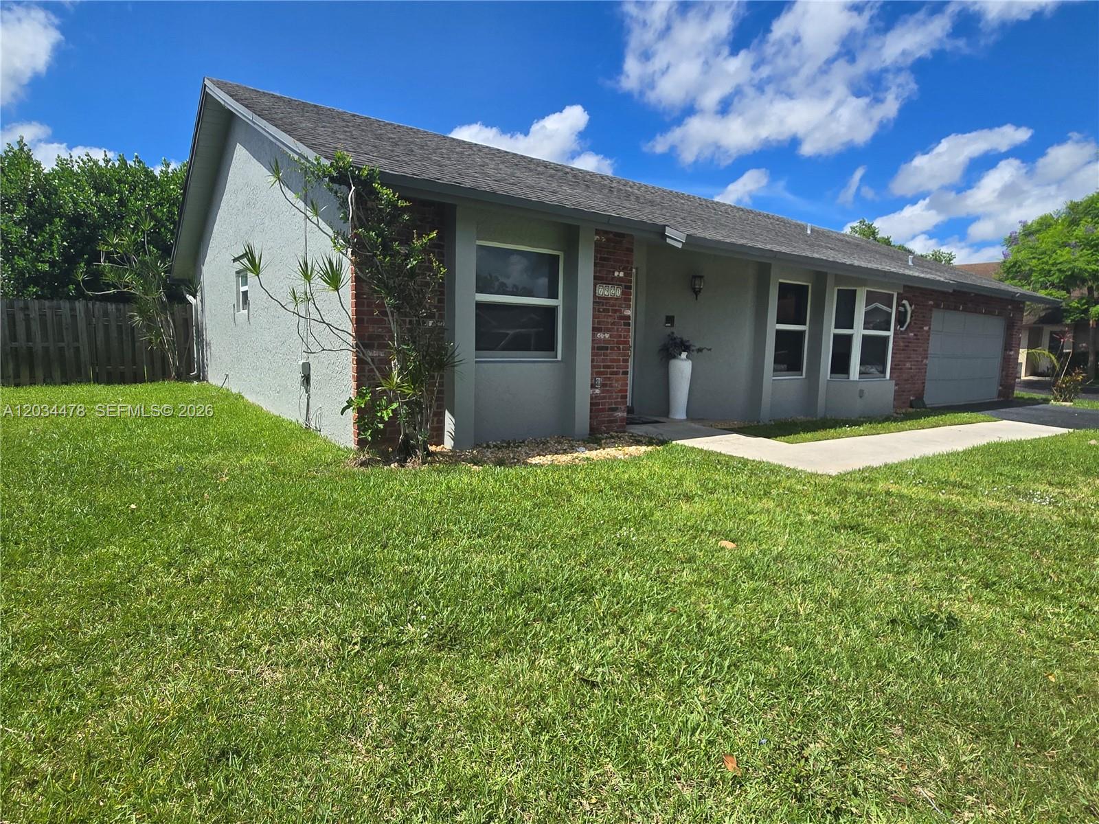 A single-story house with a gray stucco exterior, brick accents, and a shingled roof — 7921 NW 4th St, Plantation FL 33324, PLANTATION, FL