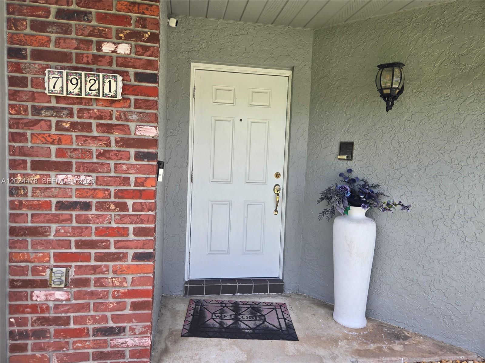 A white front door is set in a gray stucco wall next to a brick facade — 7921 NW 4th St, Plantation FL 33324, PLANTATION, FL