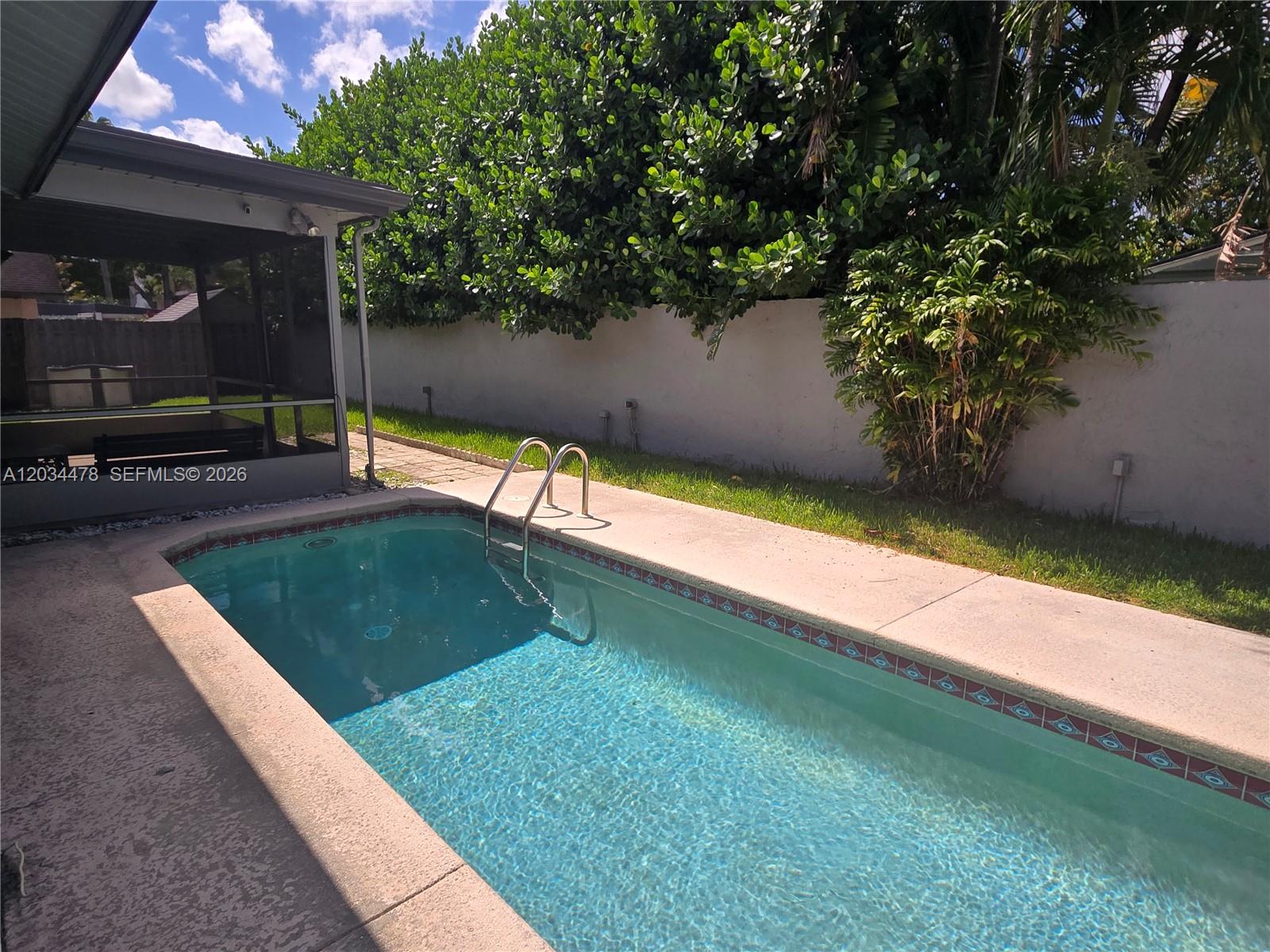 A rectangular swimming pool with a metal ladder sits beside a screened patio and wall — 7921 NW 4th St, Plantation FL 33324, PLANTATION, FL