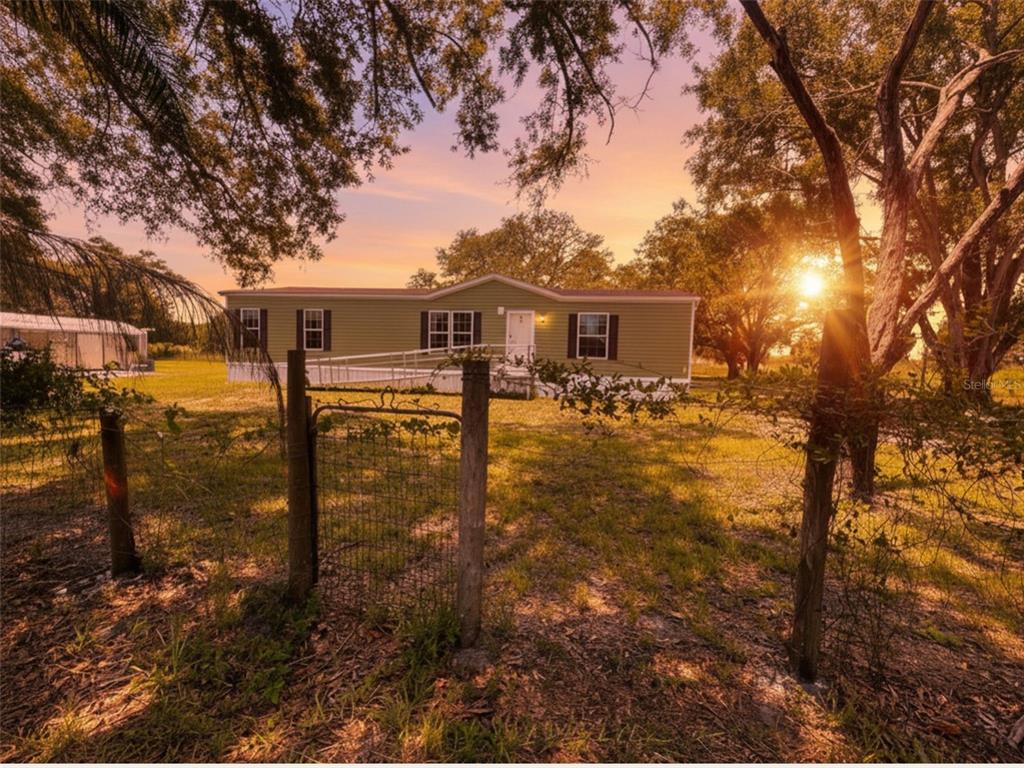 A green manufactured home sits on a grassy lot behind a wire fence at sunset — 9827 SE HOTH ROAD, ARCADIA, FL