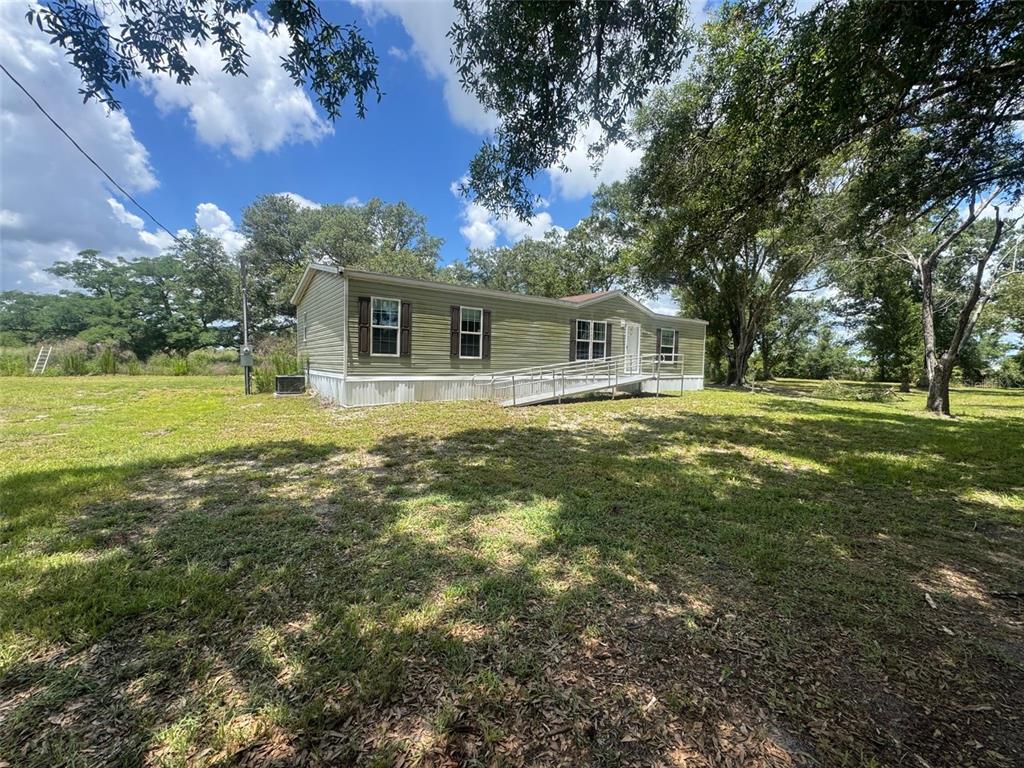 A single-story manufactured home with a metal wheelchair ramp sits on a grassy lot — 9827 SE HOTH ROAD, ARCADIA, FL