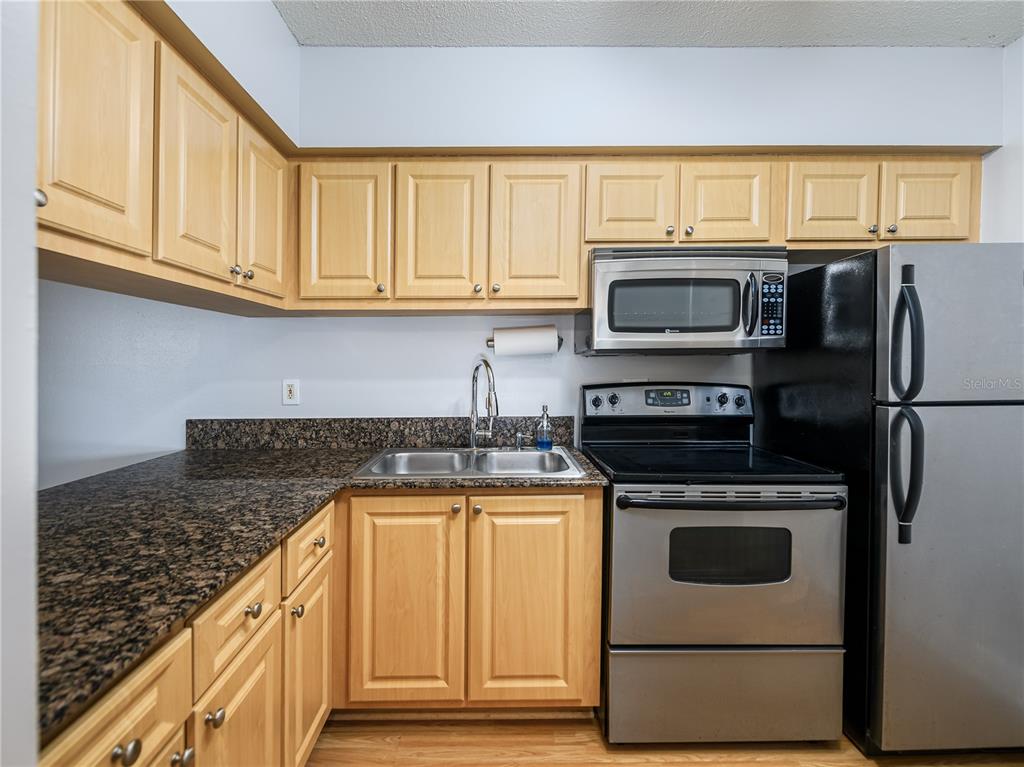 A kitchen features light wood cabinets, granite countertops, and stainless steel appliances — 120 S CHURCH AVENUE UNIT 209, TAMPA, FL