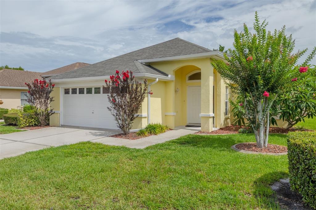 A single-story yellow house with a two-car garage and a landscaped front yard — 7843 CRAIGHURST LOOP, NEW PORT RICHEY, FL