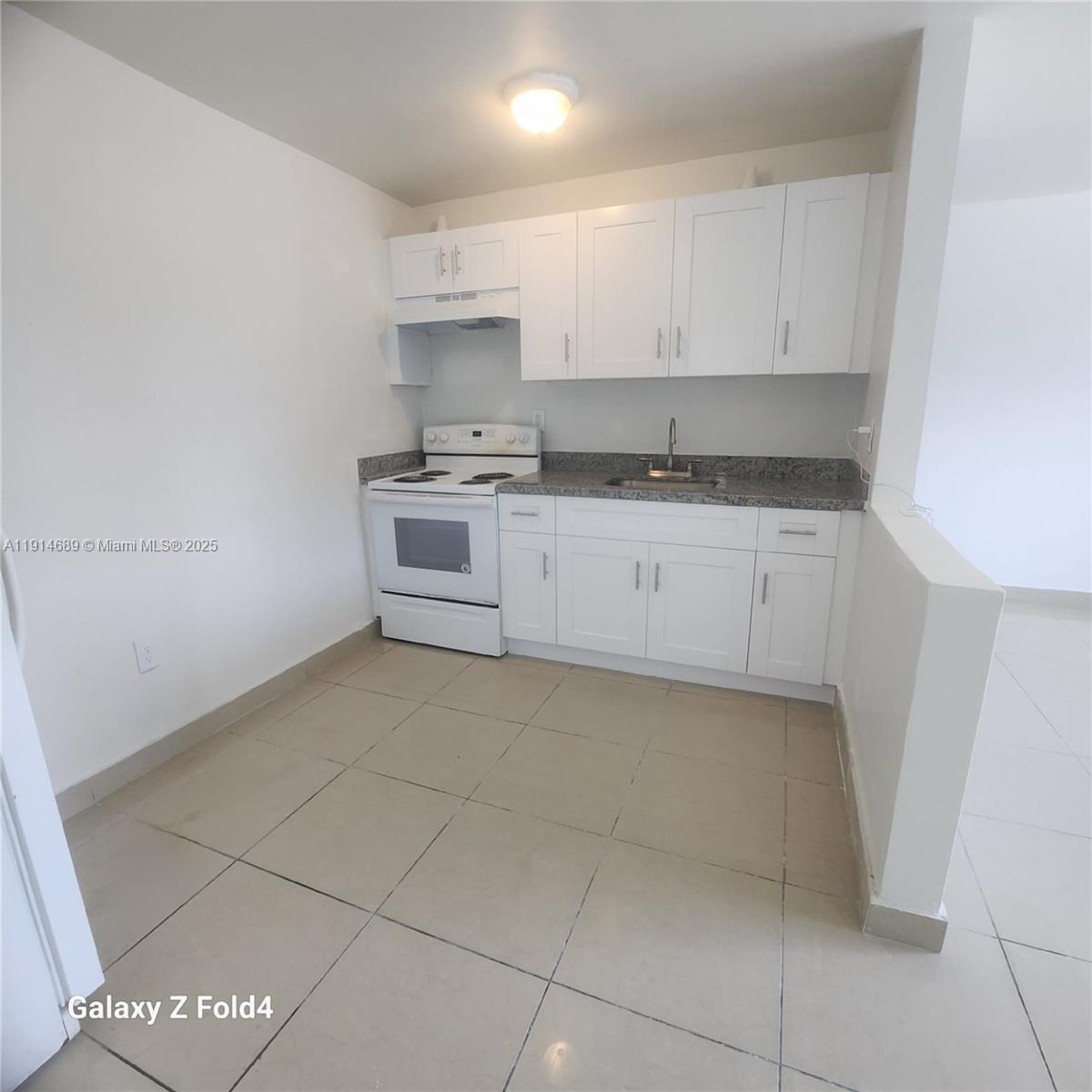 A small kitchen features white cabinets, a white stove, and gray granite countertops — 2400 NW 10th Ave # 4, Miami FL 33127, MIAMI, FL