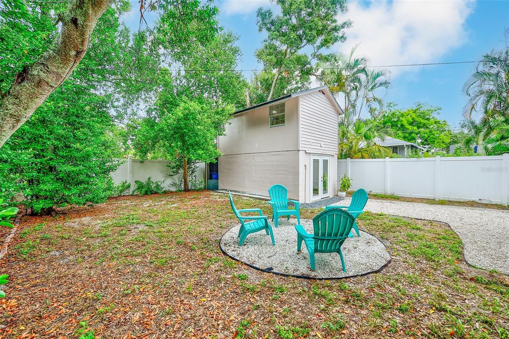 A two-story detached structure sits in a backyard with four teal chairs on gravel — 440 22ND STREET N, ST PETERSBURG, FL