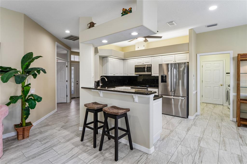 A kitchen features white cabinets, black granite countertops, stainless steel appliances, and tile flooring — 14465 MIDDLE FAIRWAY DRIVE, SPRING HILL,, FL