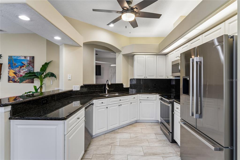 A kitchen with white cabinets and black countertops overlooks an open-concept living area with tile floors — 14465 MIDDLE FAIRWAY DRIVE, SPRING HILL,, FL
