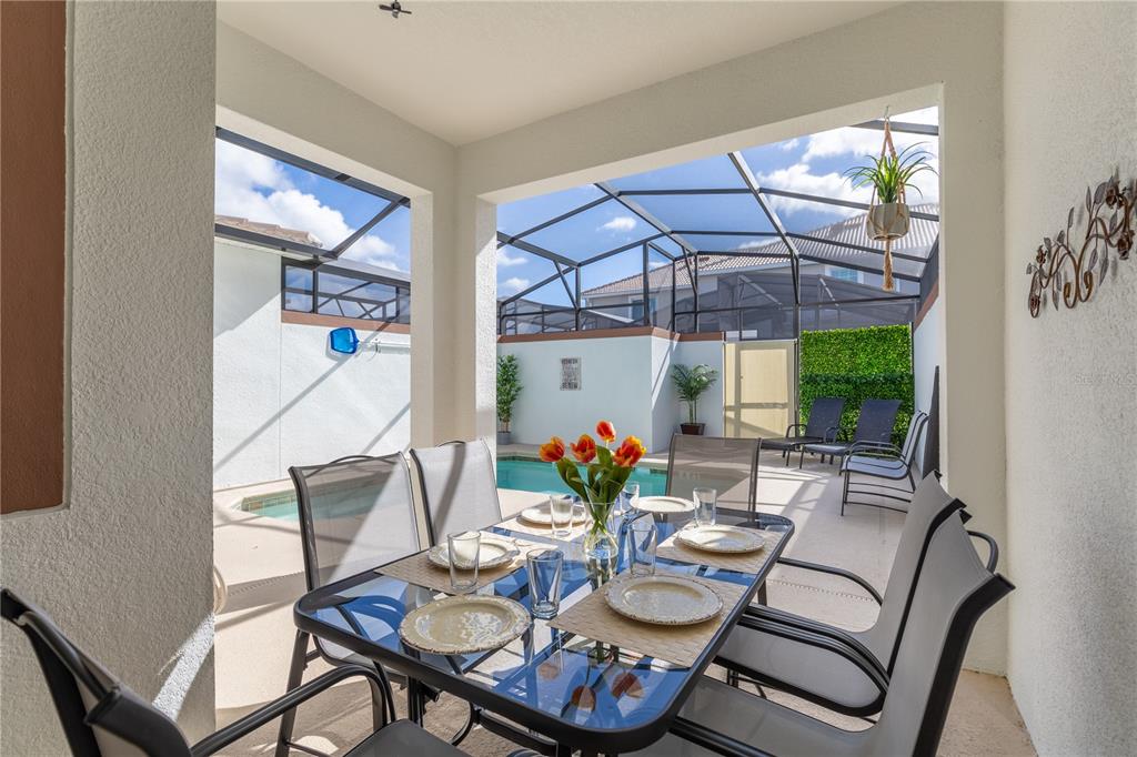 A covered patio features a glass-top dining table overlooking a screened-in pool area — 4802 LOVE STOREY LANE, KISSIMMEE, FL