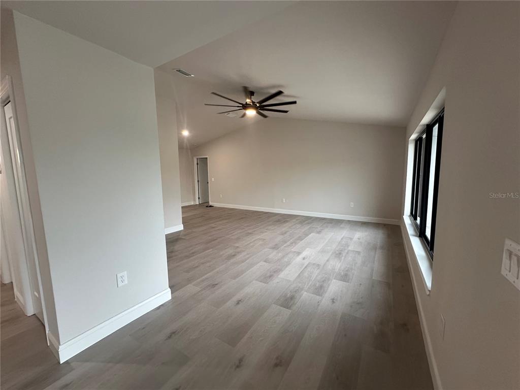 An empty room features light wood-look flooring, a ceiling fan, and large windows — 373 DORCHESTER STREET, PORT CHARLOTTE, FL