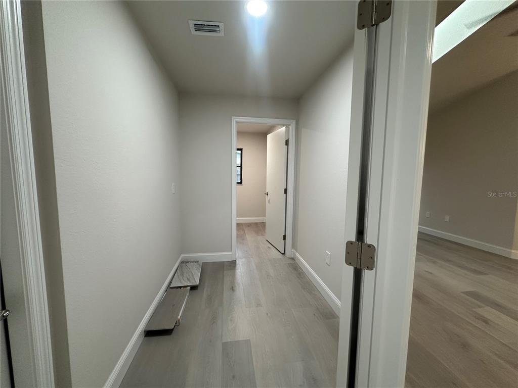 A hallway with light wood-look flooring leads to an open doorway showing another room — 373 DORCHESTER STREET, PORT CHARLOTTE, FL