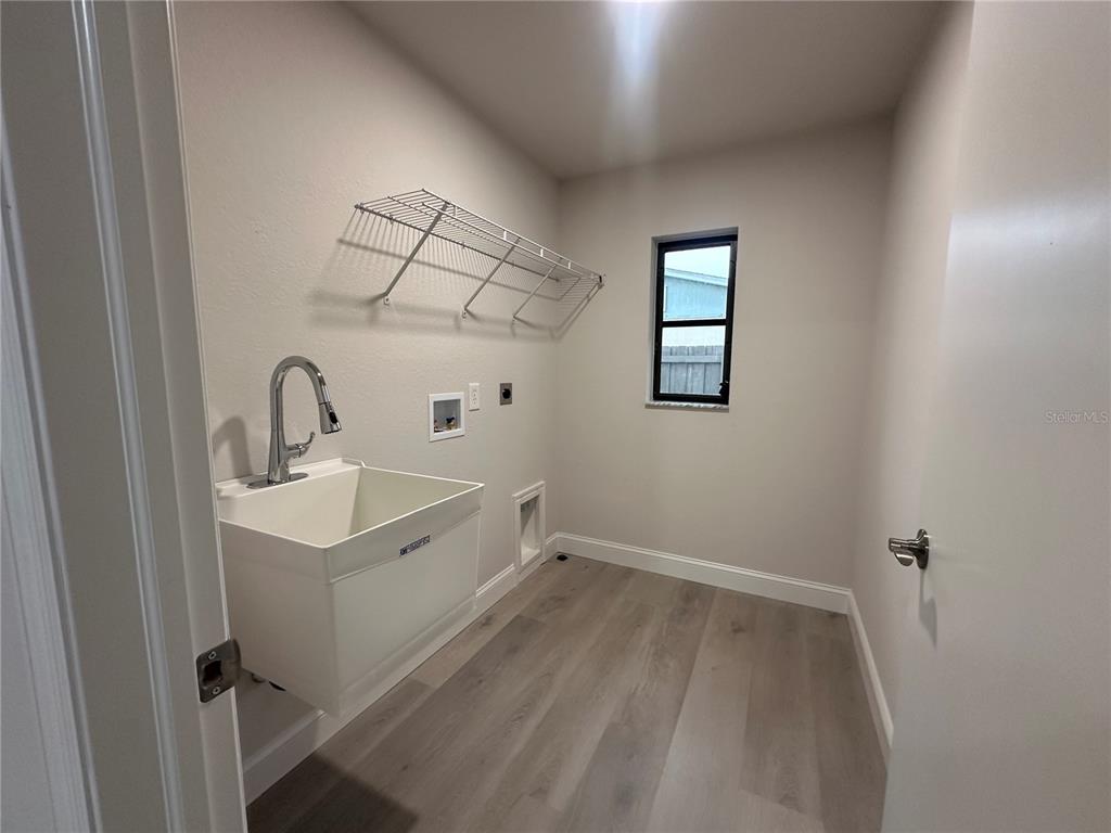 A laundry room features a utility sink, wire shelving, and light wood-look flooring — 373 DORCHESTER STREET, PORT CHARLOTTE, FL