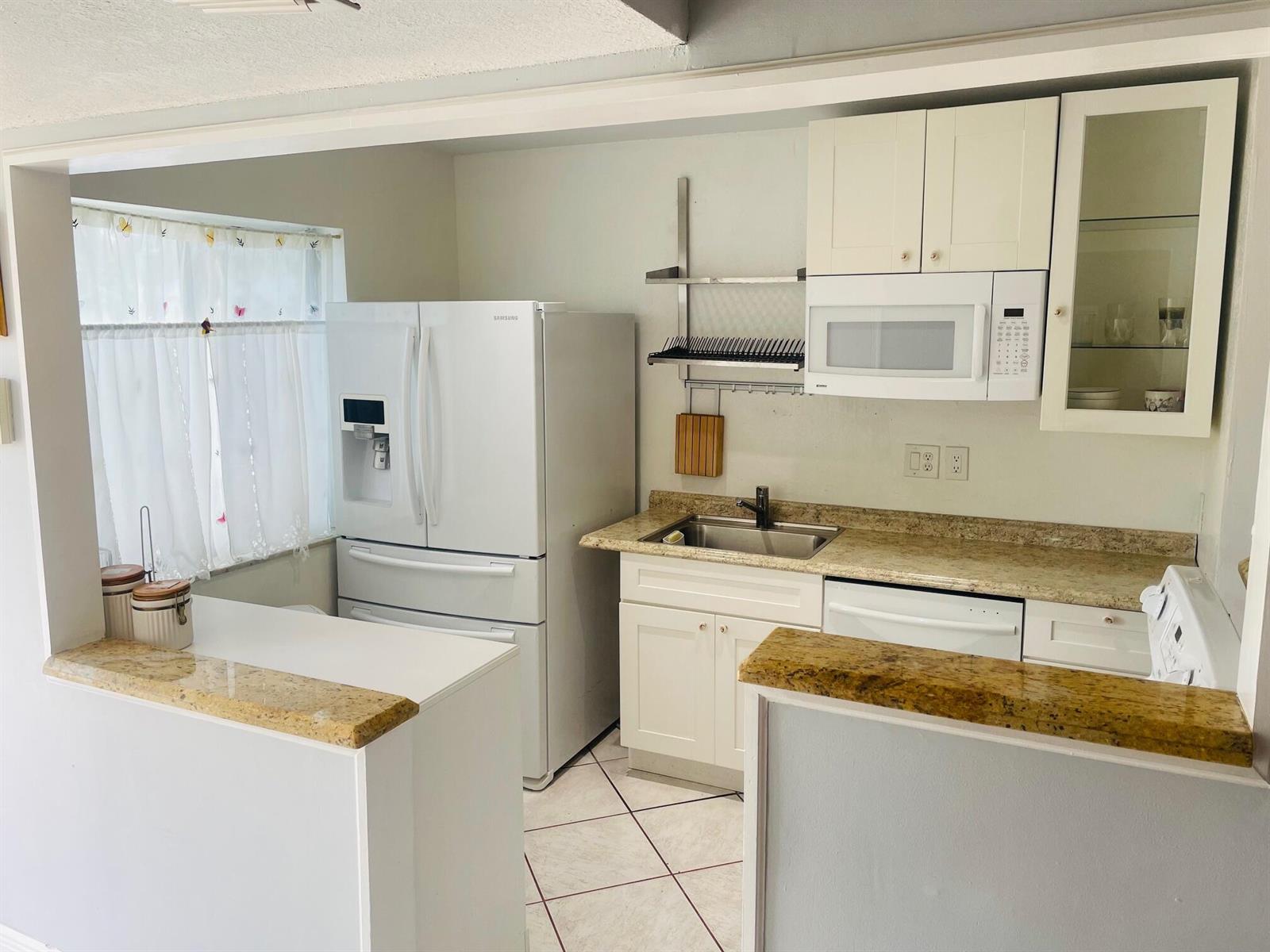 A kitchen features white cabinetry, granite countertops, a stainless steel sink, and white appliances — 139 Sparrow Drive # 2c, Royal Palm Beach FL 33411, ROYAL PALM BEACH, FL