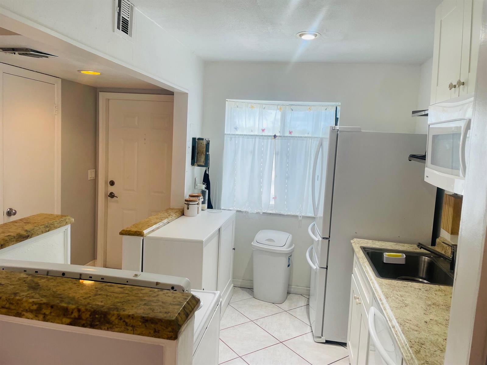 A kitchen features white cabinets, granite countertops, a white refrigerator, and a window with curtains — 139 Sparrow Drive # 2c, Royal Palm Beach FL 33411, ROYAL PALM BEACH, FL