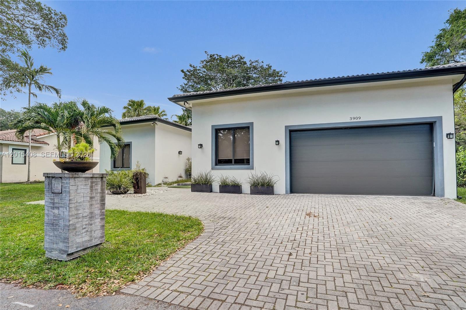 A modern single-story house features a gray garage door and a paved driveway — 3909 SW 54th Ct, Dania Beach FL 33312, DANIA BEACH, FL