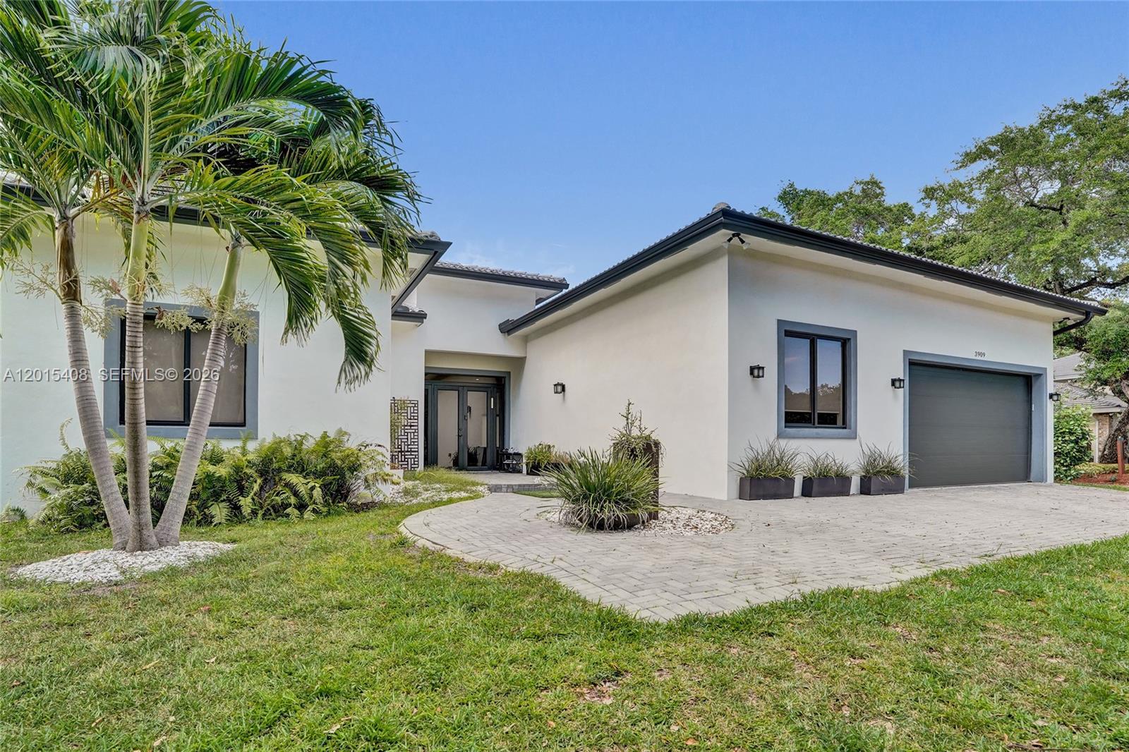 A modern single-story house features a paved driveway, palm trees, and a dark-trimmed garage — 3909 SW 54th Ct, Dania Beach FL 33312, DANIA BEACH, FL