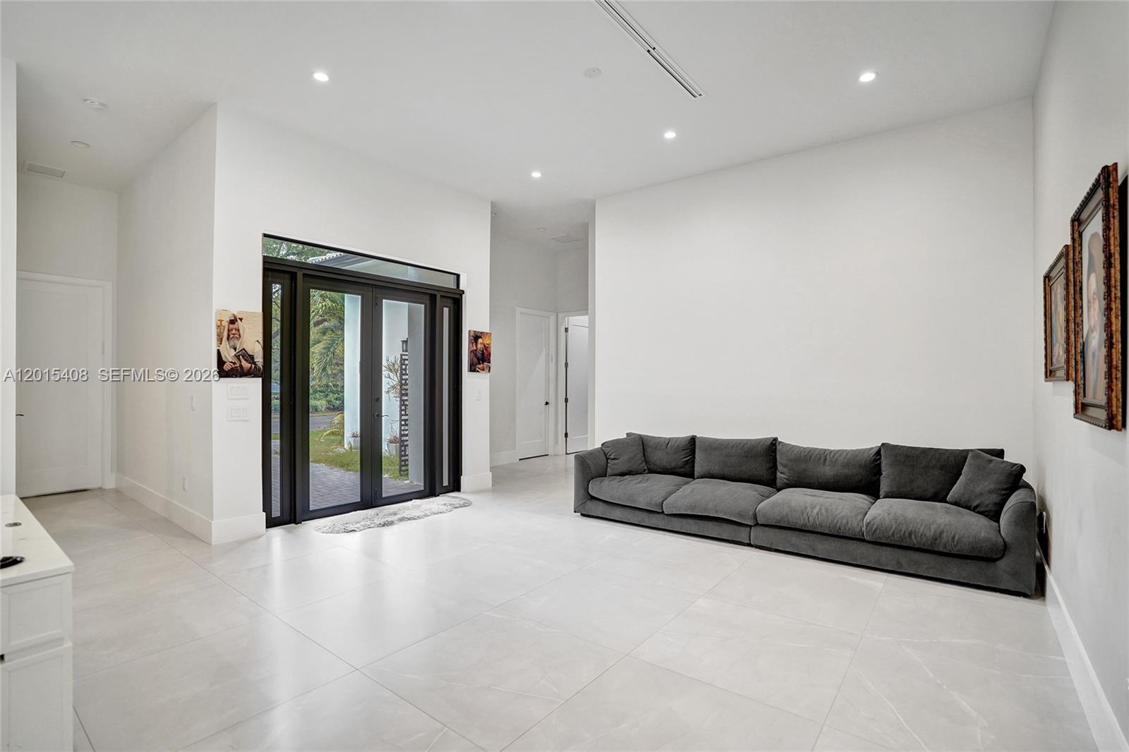 A minimalist living room features white tile floors, a large grey sofa, and double glass doors — 3909 SW 54th Ct, Dania Beach FL 33312, DANIA BEACH, FL