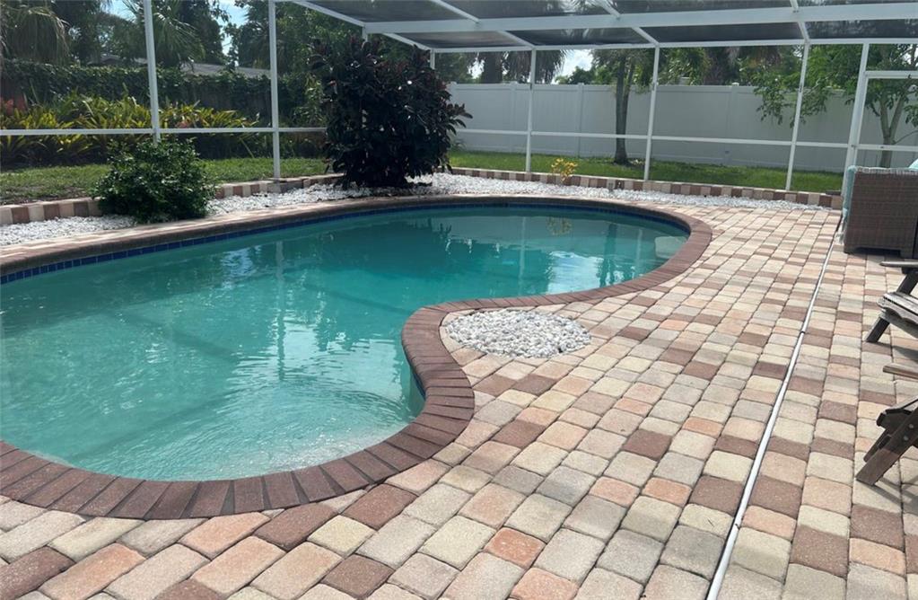 A kidney-shaped swimming pool with a brick paver deck inside a screened-in pool enclosure — 3115 BAY DRIVE, BRADENTON, FL