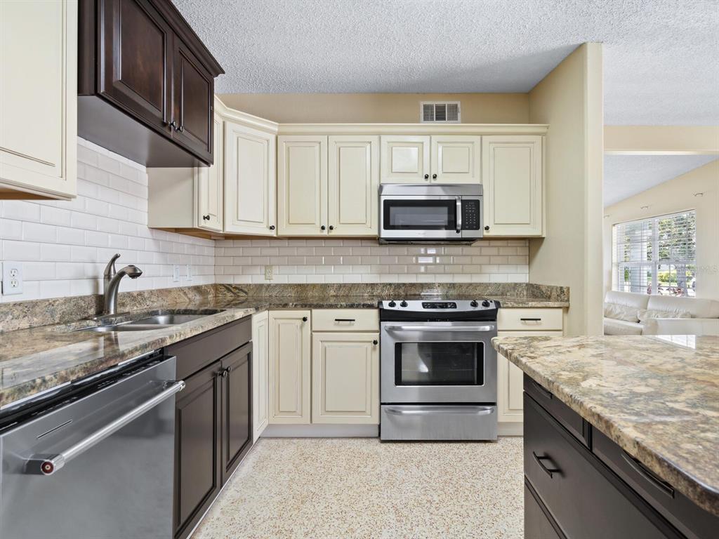 A kitchen features two-toned cabinetry, granite countertops, stainless steel appliances, and a subway tile backsplash — 3115 BAY DRIVE, BRADENTON, FL