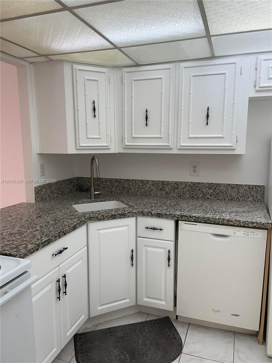 A kitchen features white cabinets, granite countertops, a stainless steel faucet, and a dishwasher — 851 Three Islands Blv # 414, Hallandale Beach FL 33009, HALLANDALE BEACH, FL