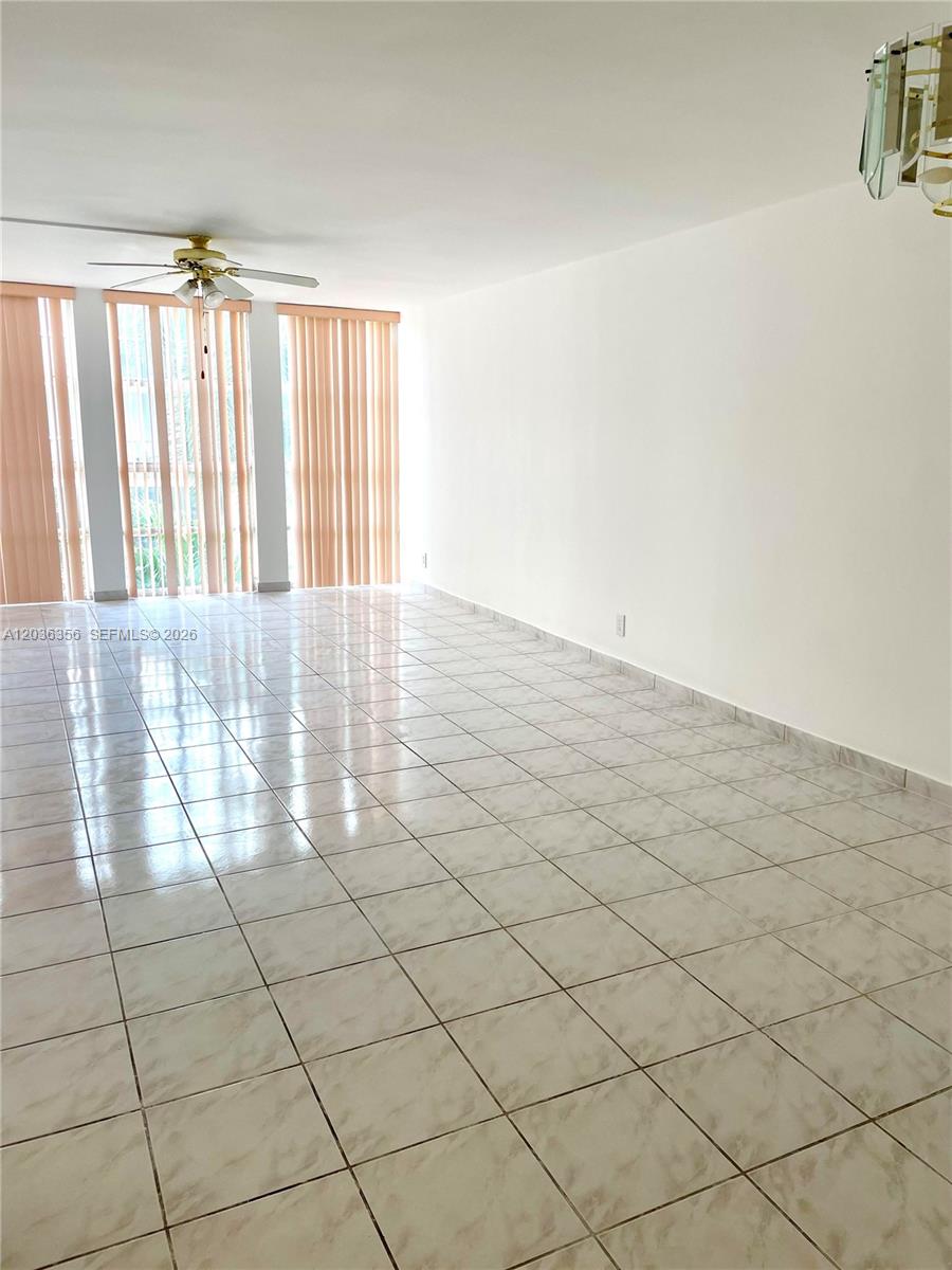 A spacious room features light-colored tile flooring, a ceiling fan, and vertical window blinds — 851 Three Islands Blv # 414, Hallandale Beach FL 33009, HALLANDALE BEACH, FL