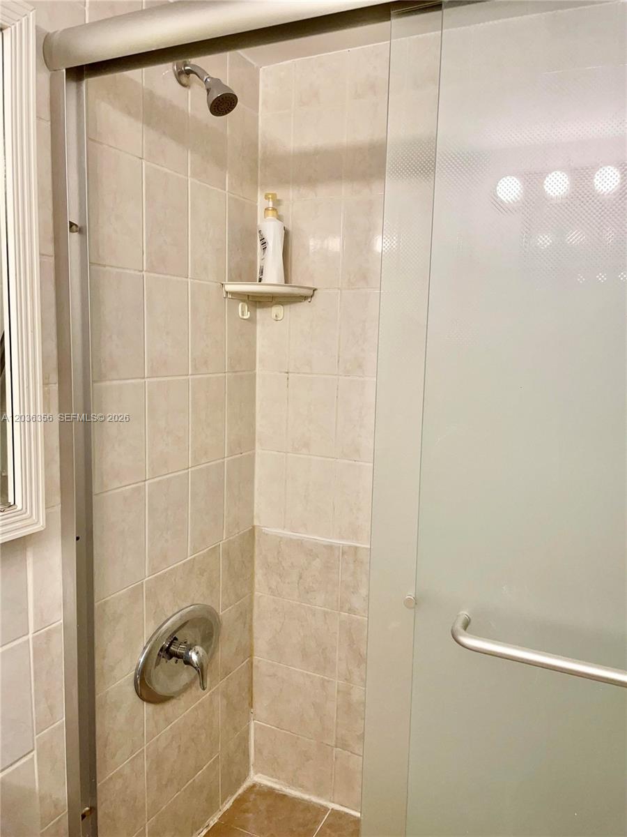 A tiled shower stall features a glass sliding door, a showerhead, and a corner shelf — 851 Three Islands Blv # 414, Hallandale Beach FL 33009, HALLANDALE BEACH, FL