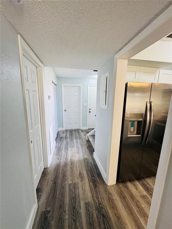 A hallway with wood-look flooring leads to two closed doors, with a stainless steel refrigerator nearby — 4100 PLAYER CIRCLE UNIT 101, ORLANDO, FL