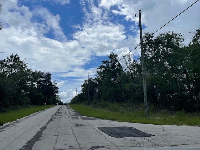 A paved road stretches toward a wooded area under a blue sky with scattered clouds — 2466 W RUTLAND DRIVE, CITRUS SPRINGS, FL