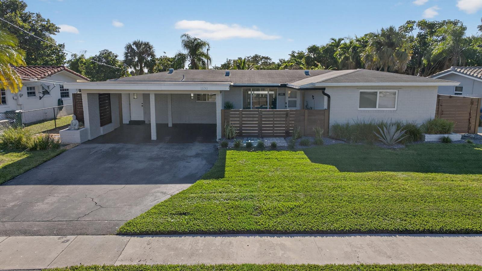 A single-story house with a light-colored brick exterior, a carport, and a wooden privacy fence — 1530 W River Drive, Margate FL 33063, MARGATE, FL