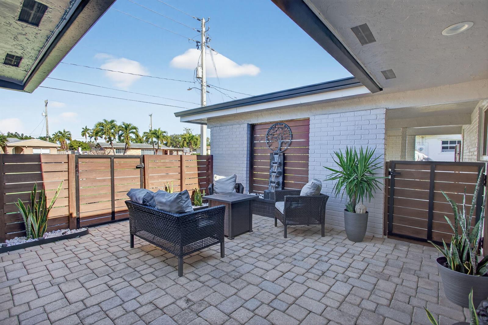 A paved outdoor patio features a fire pit, wicker furniture, and a wall-mounted water feature — 1530 W River Drive, Margate FL 33063, MARGATE, FL
