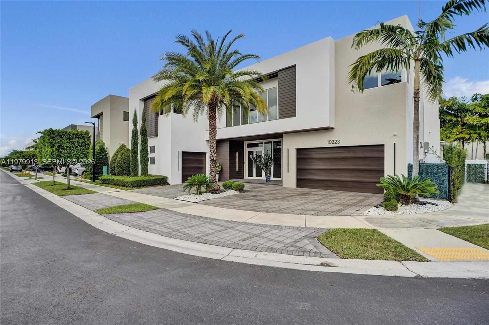 A modern two-story house features a paved driveway, a palm tree, and a dark garage — 10223 NW 75th Ter, Doral FL 33178, DORAL, FL