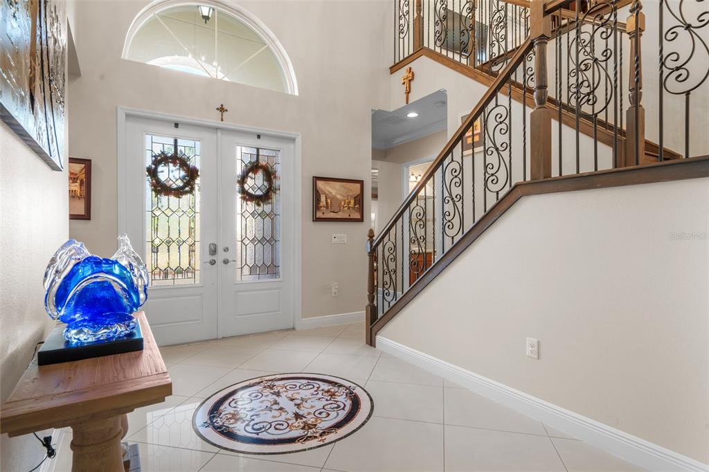 A bright foyer features a double front door, a curved staircase, and tile flooring — 30581 IVY FORGE COURT, WESLEY CHAPEL, FL