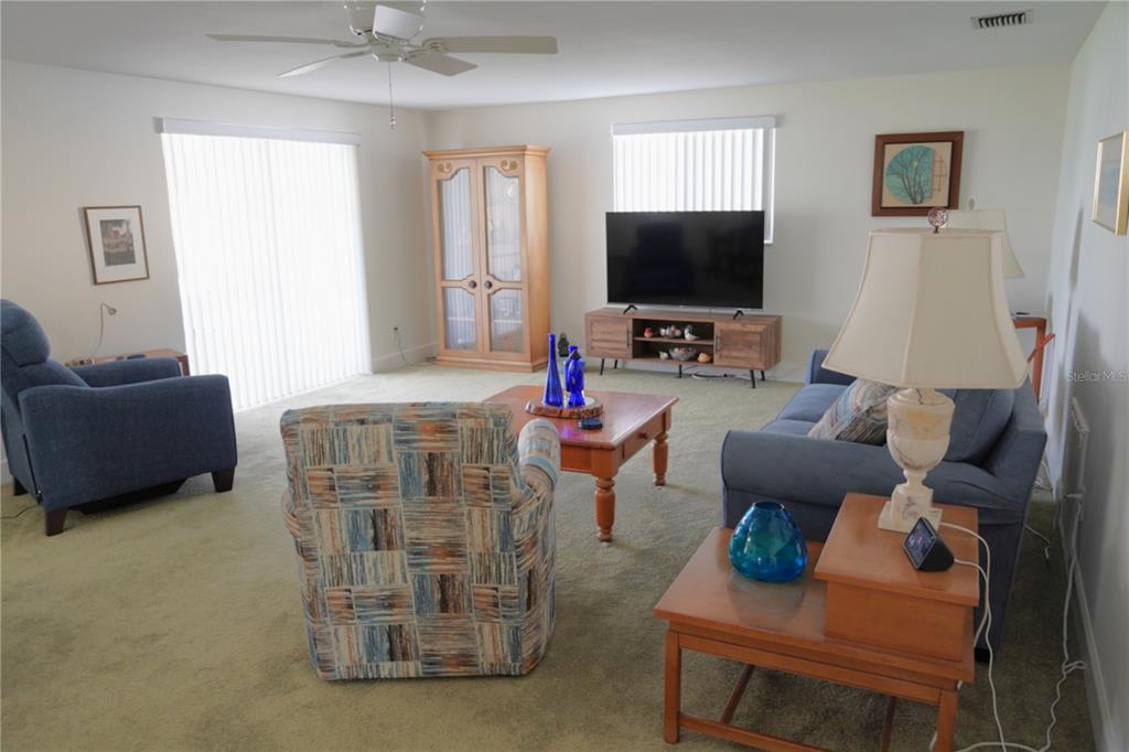 A living room with carpeted floors, a blue sofa, armchairs, a television, and a cabinet — 536 FLAMINGO DRIVE, APOLLO BEACH, FL