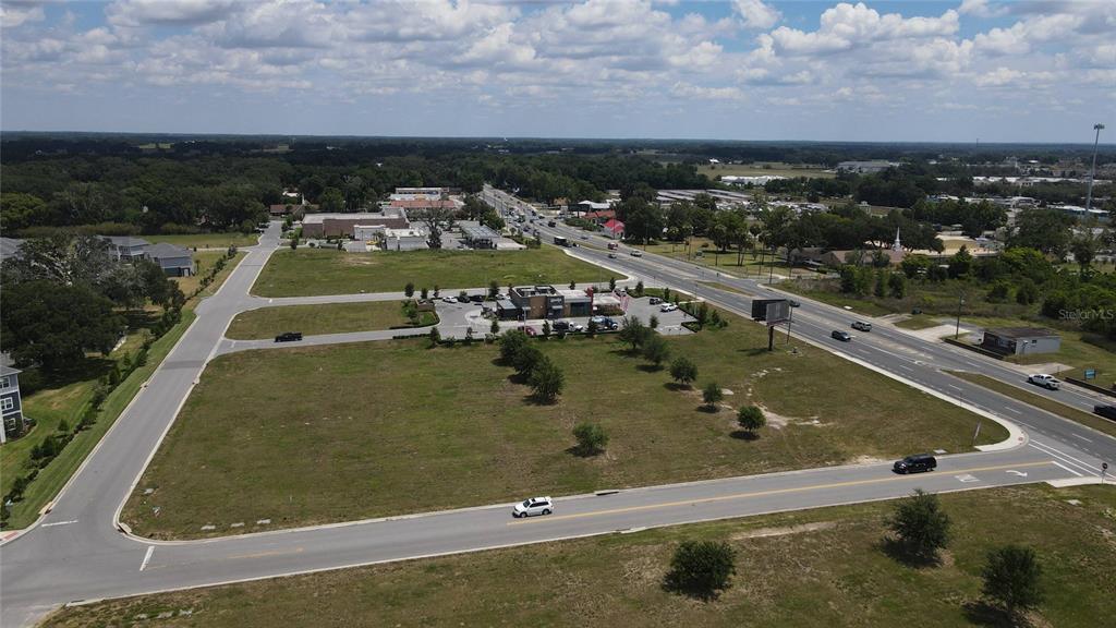 An aerial view shows a large, undeveloped grassy lot adjacent to a commercial building and roads — 11532 N US HIGHWAY 301, OXFORD, FL