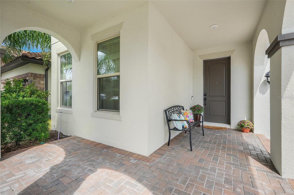 A covered front porch features brick pavers, a metal bench, and a dark entry door — 8254 PROCIDA ISLE LANE, WINDERMERE, FL