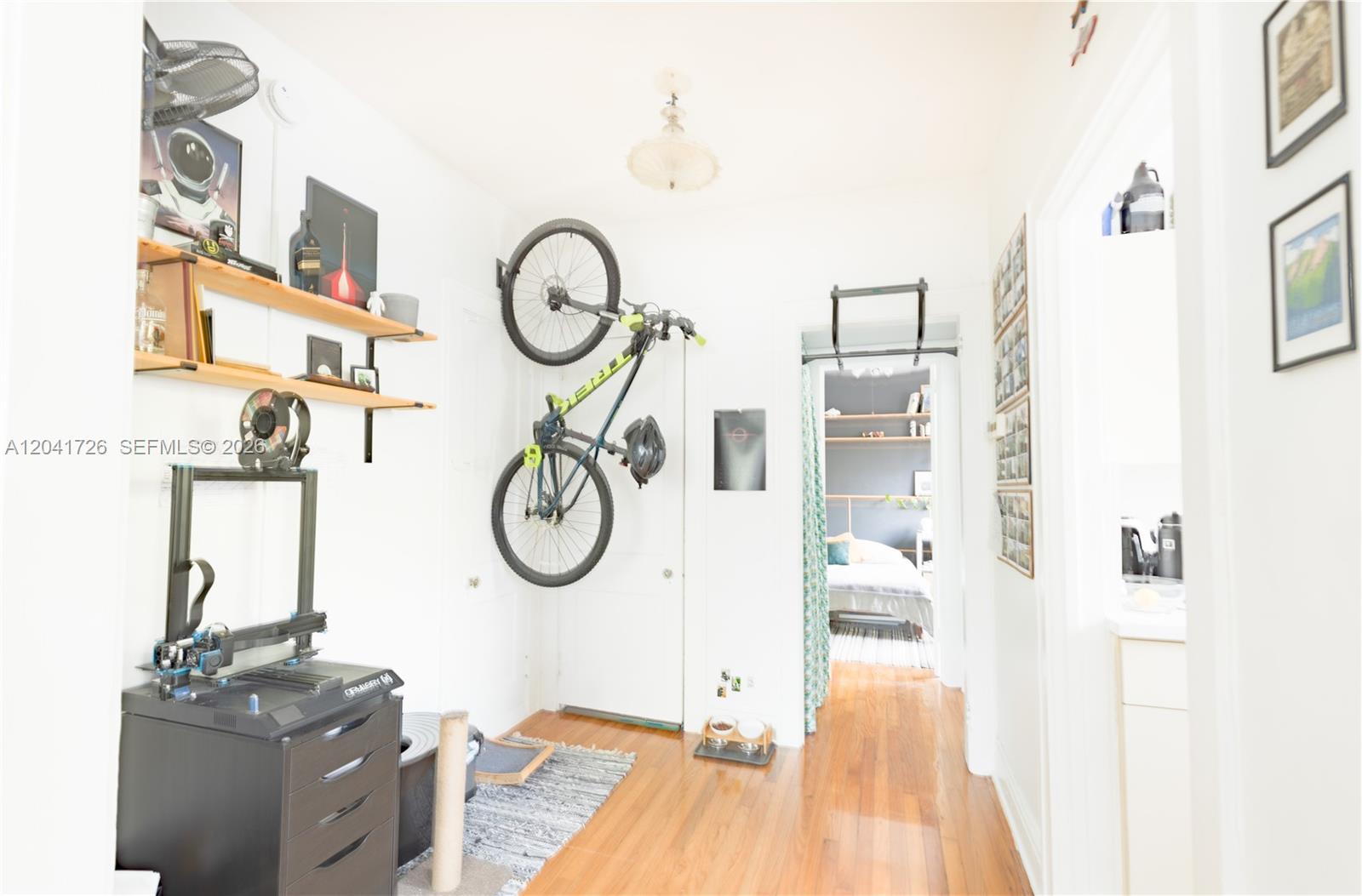 A hallway features hardwood floors, a wall-mounted bicycle, a 3D printer, and a doorway — 320 Mendoza Ave # 3, Miami FL 33134, MIAMI, FL