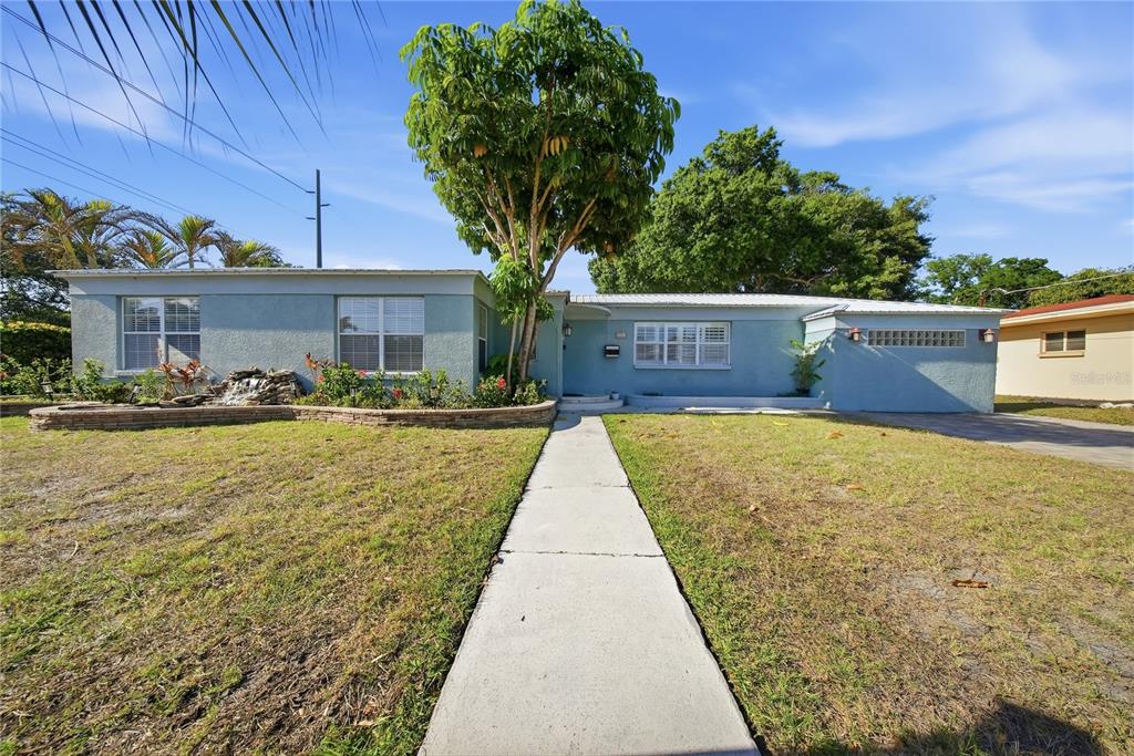 A single-story light blue house with a front walkway, a large tree, and a fountain — 3921 W BAY TO BAY BOULEVARD, TAMPA, FL