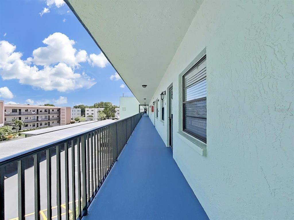 An outdoor apartment walkway with blue flooring, a black metal railing, and light-colored walls — 5973 TERRACE PARK DRIVE N UNIT 311, ST PETERSBURG, FL