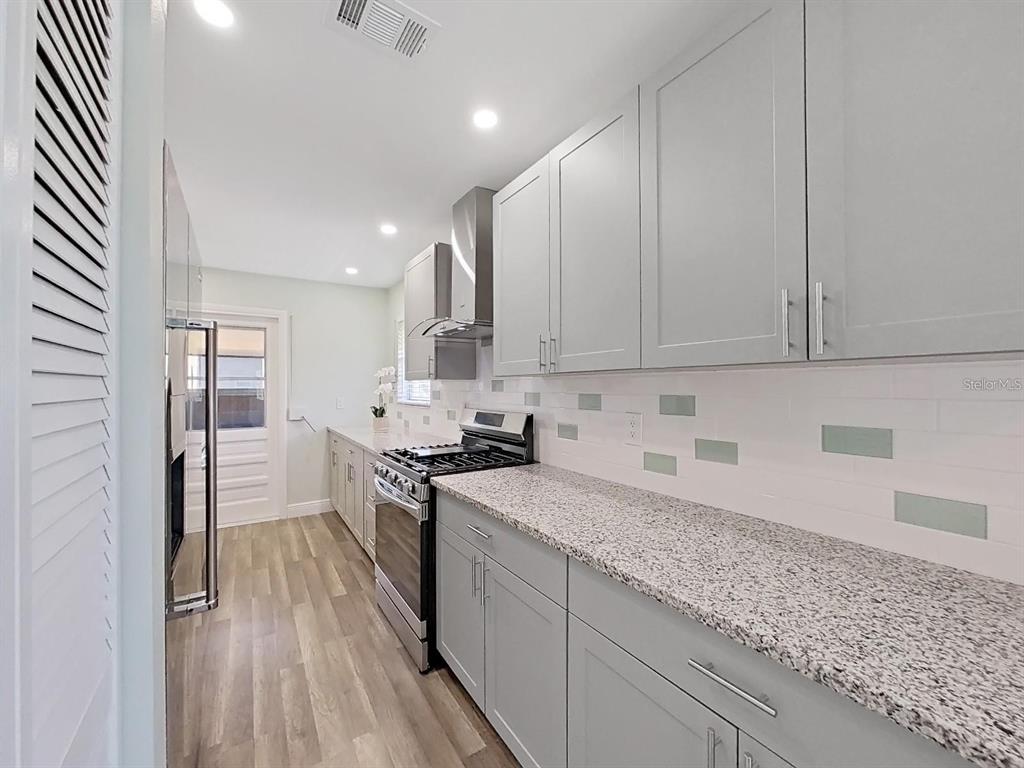 A galley kitchen features gray cabinets, granite countertops, and a stainless steel gas range — 5973 TERRACE PARK DRIVE N UNIT 311, ST PETERSBURG, FL